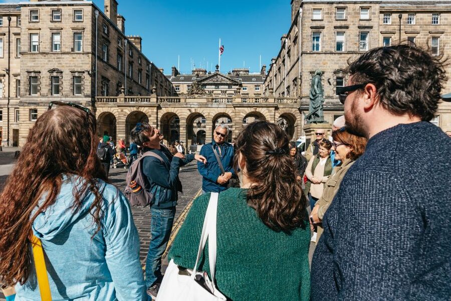 A guide with a folder of photographs stopping a group in a historic street